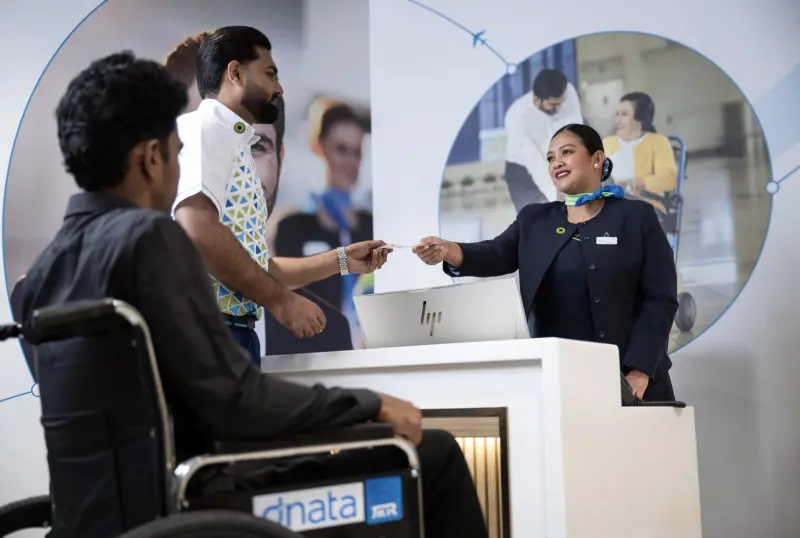 dnata ekibi tekerlekli sandalyedeki yolcuya check-in hizmeti veriyor